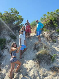 A lively group of friends enjoys a sunny day at the beach, climbing a sandy hill and capturing the moment together.