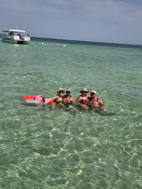 A cheerful group enjoys a refreshing swim in crystal-clear waters, sipping cocktails and soaking up the sun — a perfect beach day experience.