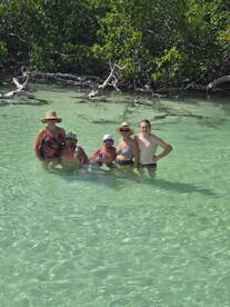 A cheerful group enjoys a refreshing swim in clear waters surrounded by mangroves, capturing the essence of a fun day on the water.