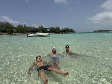 A family enjoys a fun day swimming in shallow turquoise waters, with a boat anchored nearby — perfect for a memorable sandbar stop.