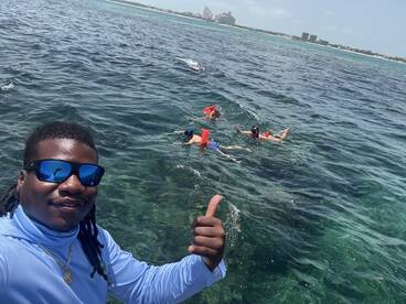 A group enjoys snorkeling in clear waters, with a friendly guide giving a thumbs up — a perfect snapshot of adventure and fun in the ocean.