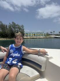 A cheerful child enjoys a boat ride in the Bahamas, with vibrant 'Bahamas' signage in the background — a perfect snapshot of family fun on the water.