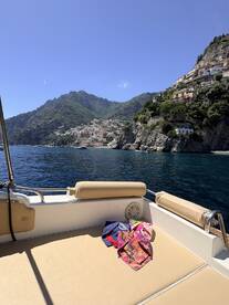 A cozy seating area on a boat, featuring colorful towels laid out, with a stunning coastal view in the background — perfect for relaxing on the water.