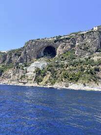 A stunning view of a coastal cliff with a natural cave and picturesque buildings, showcasing the beauty of the landscape along the water's edge.