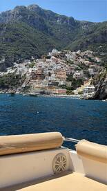 A stunning view of the colorful coastal town along the Amalfi Coast, captured from a boat, showcasing the beautiful architecture and lush mountains in the background.