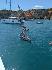 A joyful family enjoys paddleboarding in the ocean, showcasing a fun day on the water with stunning cliffs in the background.