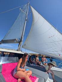 A lively group enjoys a day of sailing on a catamaran, relaxing on the deck with stunning views and good company.