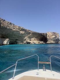 A stunning view from the bow of a boat navigating through crystal-clear waters, showcasing the dramatic cliffs and vibrant blue hues of the coastline.