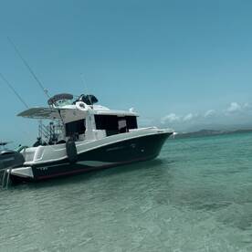 A sleek boat named 'Barracuda' anchored in shallow waters, showcasing its elegant design against a clear blue sky — perfect for a day of adventure on the water.