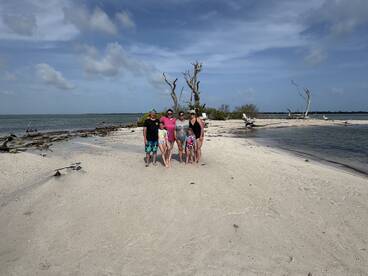 A joyful family poses together on a sandy beach, capturing a memorable moment during their sandbar adventure — perfect for family outings and beach fun.