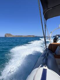 A scenic view from a boat cruising through clear blue waters, showcasing a distant island against a vibrant sky — perfect for adventure seekers and nature lovers.