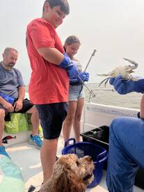 A joyful family engages in crabbing on a boat, with kids actively participating and a dog watching eagerly — a perfect day of fishing fun on the water.