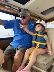 A heartwarming moment aboard a boat as a child in a life jacket points excitedly while sitting next to an adult, showcasing the joy of family boating adventures.