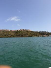 A picturesque view of a coastline with lush hills and colorful buildings, showcasing the beauty of the harbor area — perfect for scenic boat tours.