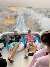 A group of friends relaxes on bean bags aboard a boat, enjoying drinks and the scenic water view — perfect for a fun day on the water.