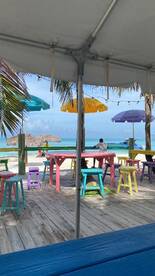 A vibrant beachside scene featuring colorful tables and umbrellas, with a person seated, creating a relaxed atmosphere perfect for enjoying the ocean view.