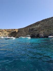 A vibrant scene in Malta showcasing multiple boats anchored near a stunning rocky coastline, with people enjoying the clear turquoise waters — a perfect destination for swimming and exploration.