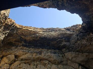 An unclear view of a rocky cave opening against a bright blue sky, lacking identifiable features or subjects.