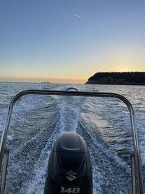 A striking view from the back of a speedboat cruising through calm waters at sunset, showcasing the engine and wake trailing behind.