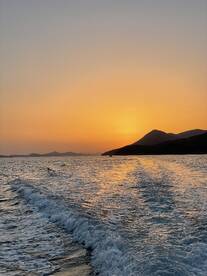 A stunning sunset over the coastline, with gentle waves reflecting the warm hues of the evening sky — a perfect backdrop for a serene boating experience.