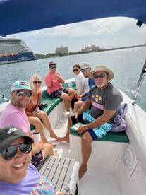 A lively group enjoys their time aboard a boat, capturing the fun of a day on the water with drinks and laughter, set against a backdrop of a cruise ship and tropical scenery.
