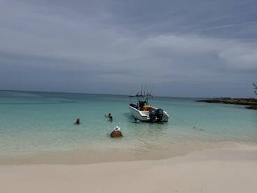 A group enjoys a fun day at the beach, swimming near a boat anchored in the clear waters — perfect for family outings and water adventures.