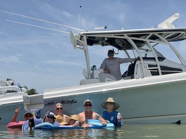 A lively group enjoys a fun day in the water, relaxing on floats while the boat is anchored nearby — perfect for summer outings and social gatherings.