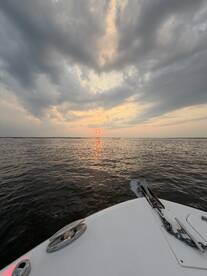 A serene sunset view from the bow of a boat, showcasing the tranquil waters and dramatic sky — perfect for romantic evening cruises.