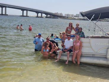 A lively group enjoys a fun day at the sandbar, swimming and relaxing around a pontoon boat, creating unforgettable summer memories.