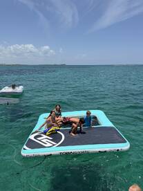A group of children enjoys a sunny day on a floating mat in clear turquoise waters, perfect for summer fun and water activities.