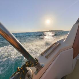 A stunning view from the side of a boat cruising through sparkling waters, with the sun setting on the horizon — perfect for showcasing the beauty of a day on the water.