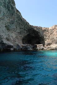 A stunning view of a rocky coastline with a cave entrance, surrounded by crystal-clear turquoise waters — an ideal spot for exploration and adventure.