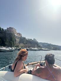 A couple enjoys a relaxing moment on a boat, surrounded by scenic coastal views and other vessels, perfect for a day out on the water.