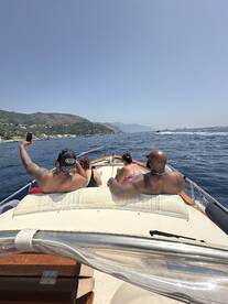 A group of friends enjoys a sunny day on the water, capturing memories aboard a boat with stunning coastal views in the background.