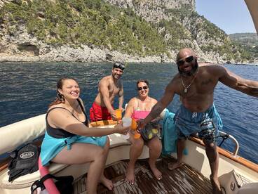 A lively group enjoys cocktails on a boat, celebrating together against a stunning coastal backdrop — perfect for memorable summer outings.