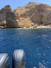 A clear view of the boat's outboard motors with a rugged rocky coastline in the background, showcasing the beauty of the surrounding waters.