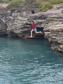 A young boy joyfully leaps off a cliff into the clear turquoise waters, capturing the thrill of adventure and summer fun.