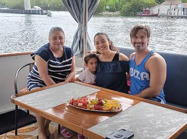 A joyful family gathers around a table on a boat, enjoying a colorful spread of fresh fruits — perfect for a relaxing day on the water.