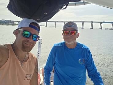 Two men enjoy a sunny day on the water, capturing a moment aboard their boat with a scenic backdrop of a bridge. Perfect for showcasing camaraderie and boating adventures.