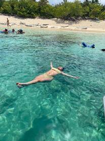 A woman floats in the crystal-clear waters while others enjoy the beach, capturing the essence of a perfect day in paradise.