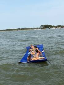 A lively group enjoys a day on a floating mat, sipping drinks and soaking up the sun — a perfect summer party on the water.
