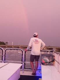 A person enjoys a serene moment on a boat, gazing at a beautiful rainbow against a twilight sky — a perfect backdrop for memorable boating experiences.
