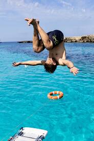 A man performs an impressive jump into the crystal-clear turquoise waters, showcasing the excitement of summer fun and water activities.