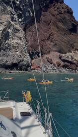A vibrant scene of kayakers exploring the stunning coastline, with a sailboat in the foreground, perfect for adventure seekers and nature lovers.