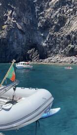A scenic view of a rocky coastline with boats in the water, showcasing a vibrant day of boating and kayaking in a beautiful natural setting.