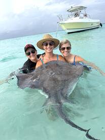 Three women interact with a stingray in shallow turquoise waters, creating a memorable wildlife experience in a tropical paradise.
