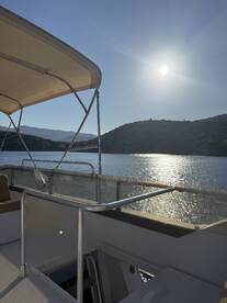 A serene view of a boat's deck under bright sunlight, showcasing the tranquil waters and surrounding hills — perfect for a peaceful day on the water.