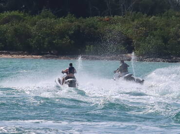 Two individuals enjoy an exhilarating ride on jet skis, creating splashes in the turquoise waters — a perfect snapshot of adventure on the water.