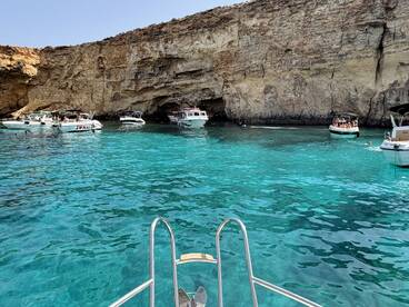 A vibrant scene at a picturesque cove in Malta, featuring multiple boats and people enjoying the crystal-clear waters — perfect for a day of swimming and exploration.