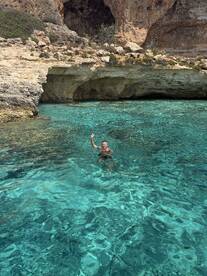 A swimmer enjoys the crystal-clear waters near a stunning cave, showcasing the beauty of outdoor adventures and exploration.